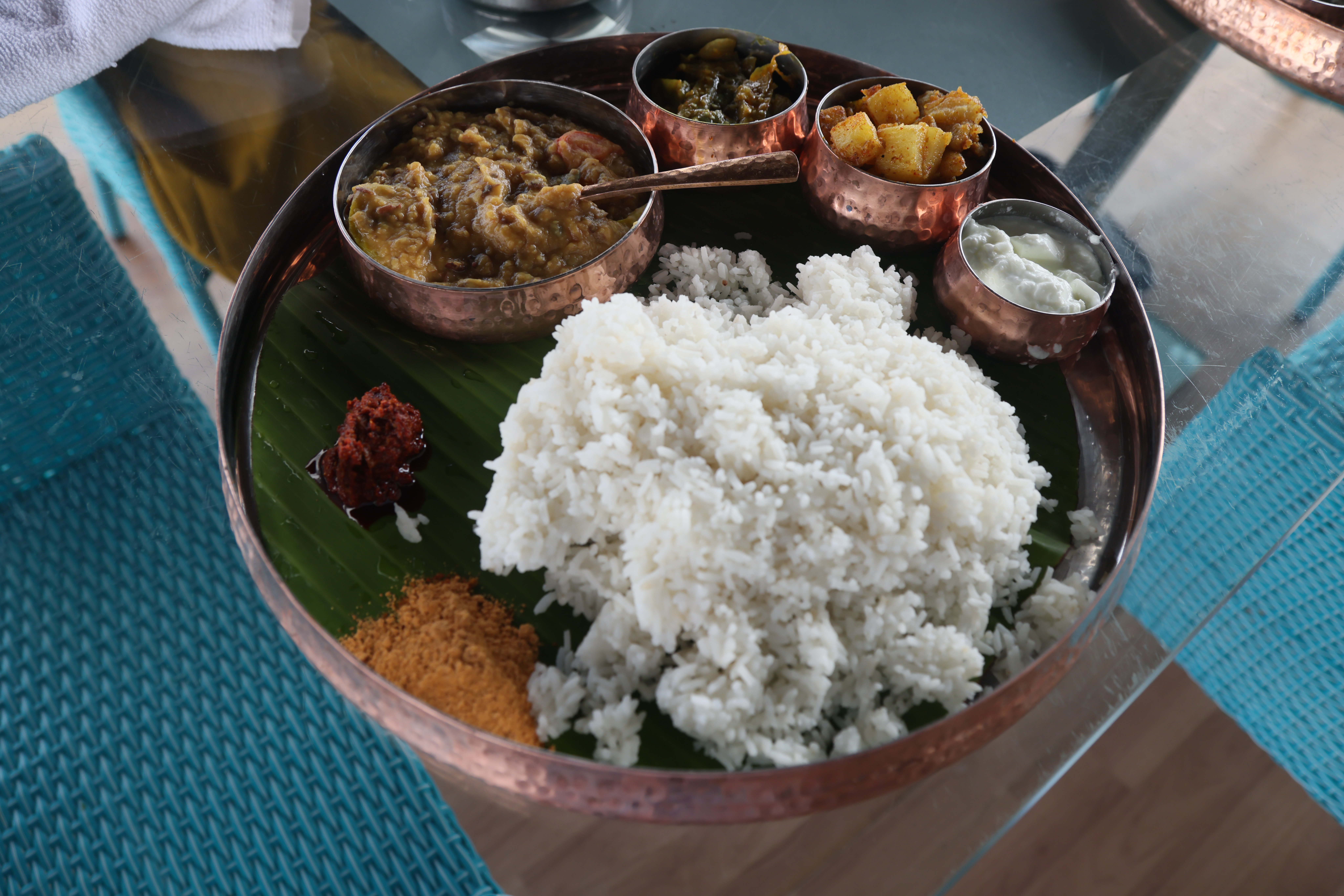 A traditional Indian meal served on a banana leaf in a copper plate.